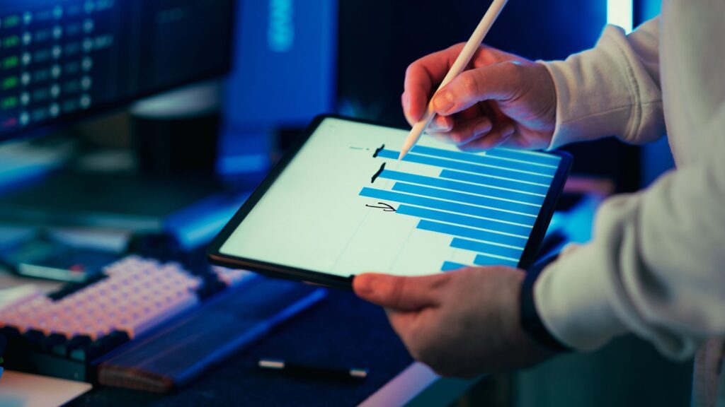 A professional analyzing a blue bar chart on a tablet screen with a stylus.