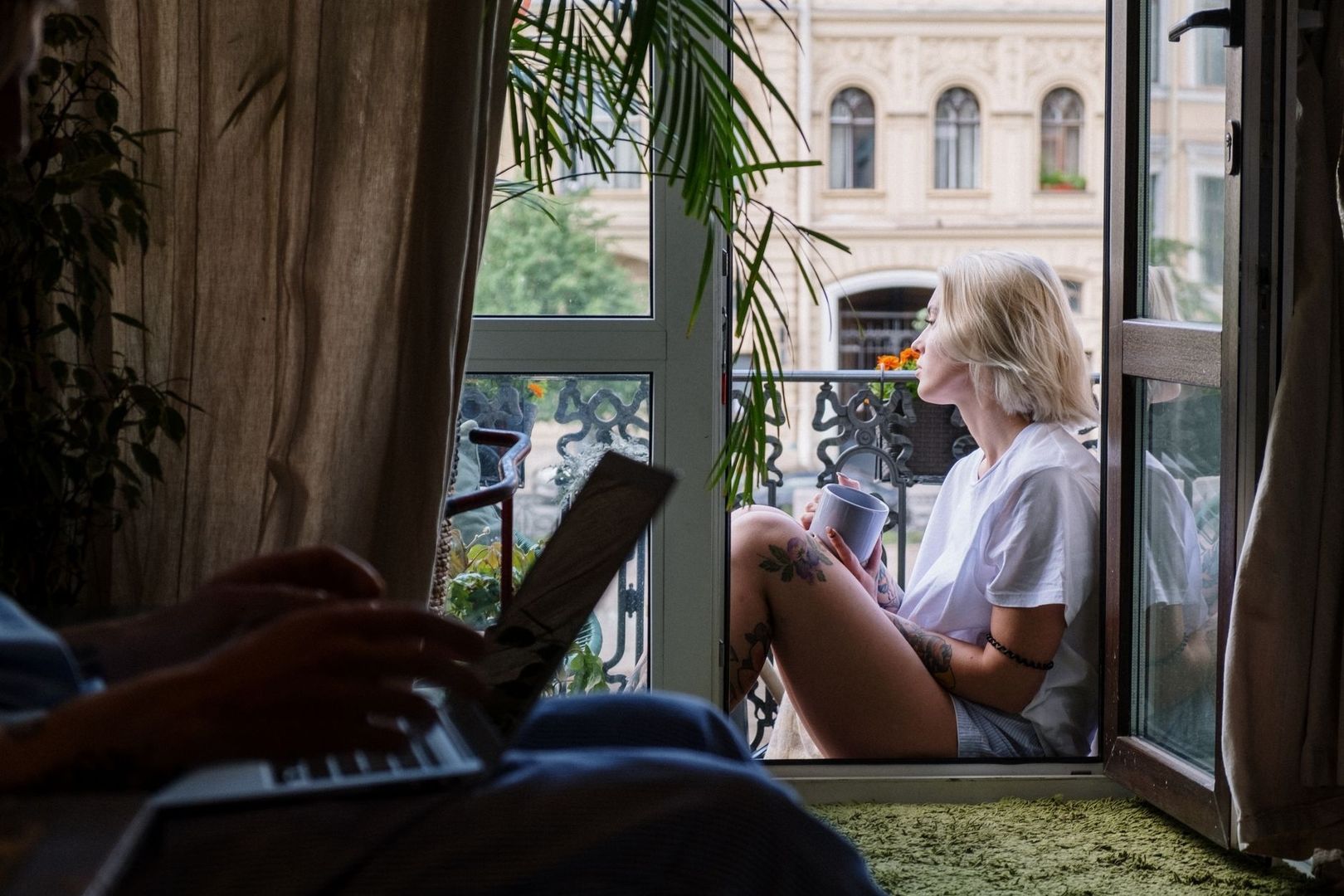Woman drinking coffee on a balcony overlooking an ornate city building